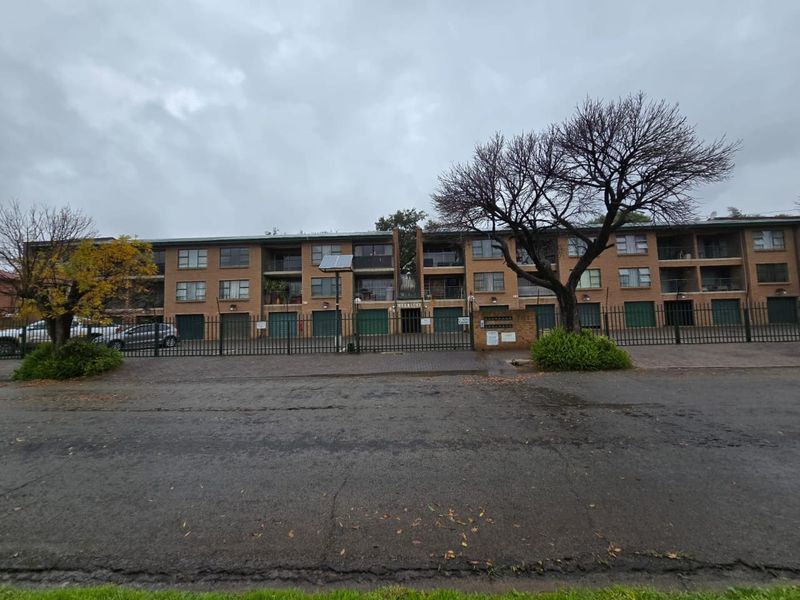 Front elevation of a multi-story brick apartment complex featuring secure perimeter fencing, ground-level garage access, and private balconies.