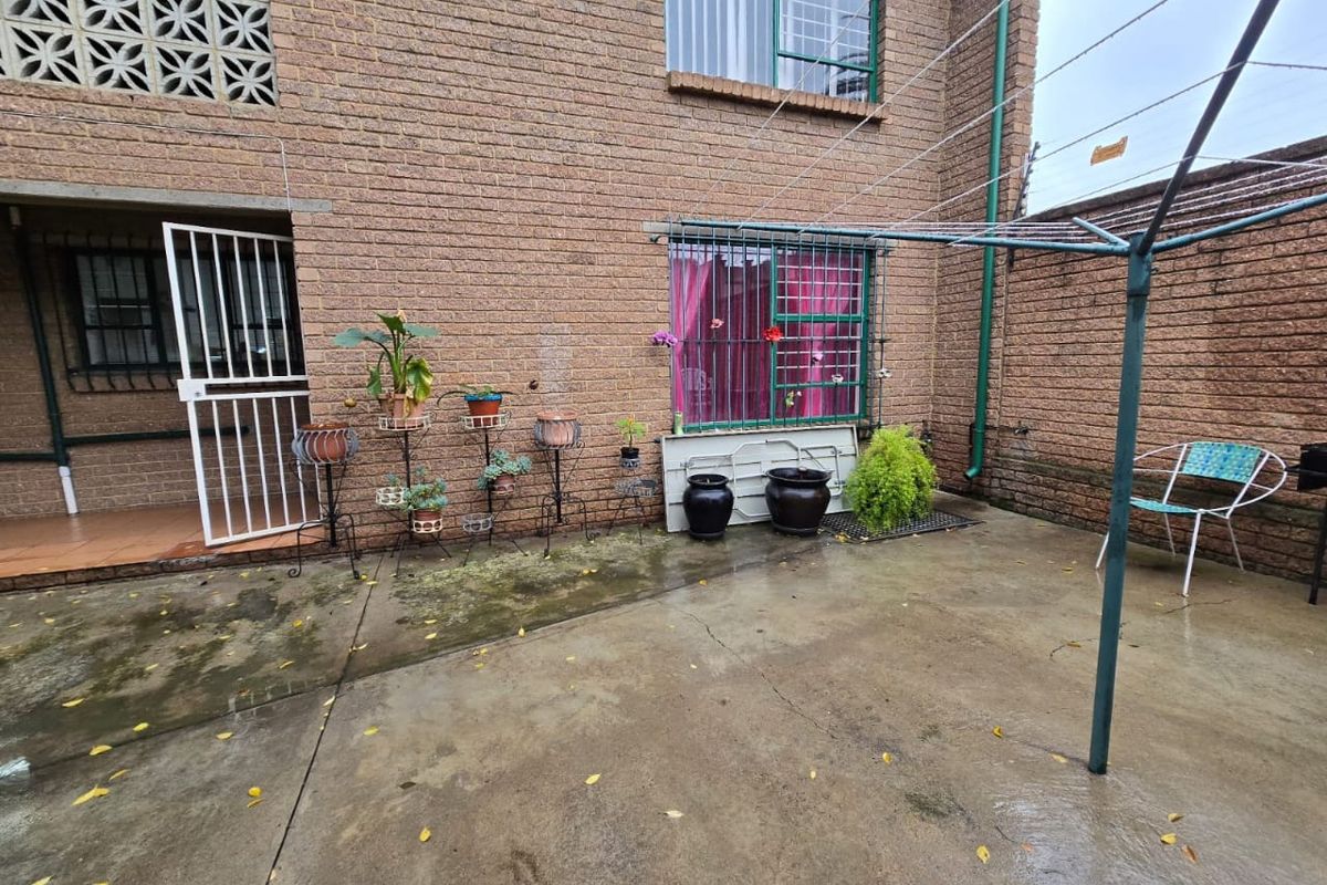 A rear exterior courtyard featuring a brick facade, concrete paving, security-barred windows, and a rotary clothesline.
