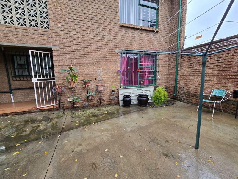 A rear exterior courtyard featuring a brick facade, concrete paving, security-barred windows, and a rotary clothesline.