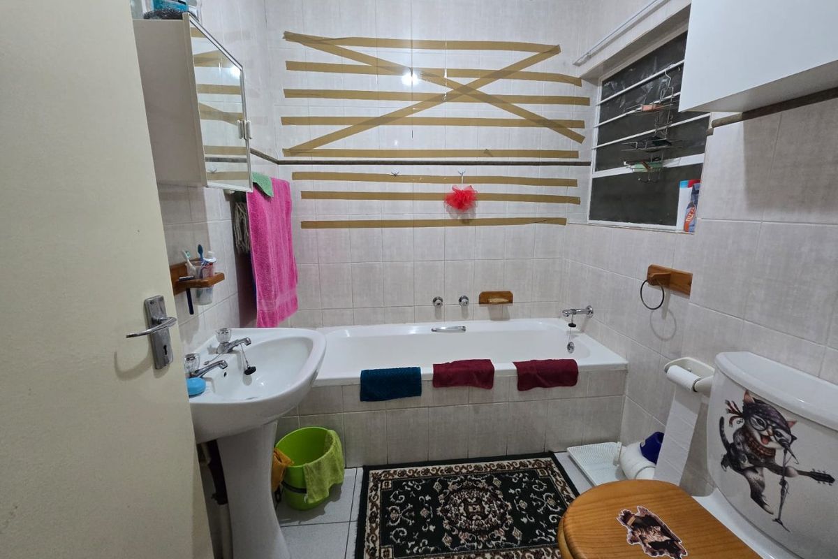A functional bathroom featuring a pedestal basin, built-in bathtub, and tiled finishes. The space requires cosmetic updates to improve its overall presentation.