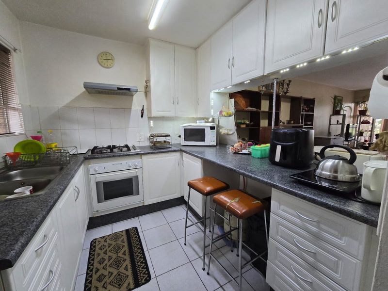 Functional kitchen featuring white cabinetry, gas hob, built-in oven, extractor fan, and a breakfast bar with tiled flooring.