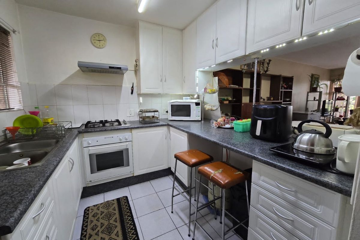 Functional kitchen featuring white cabinetry, granite countertops, a gas hob, electric oven, and a breakfast bar overlooking the living area.