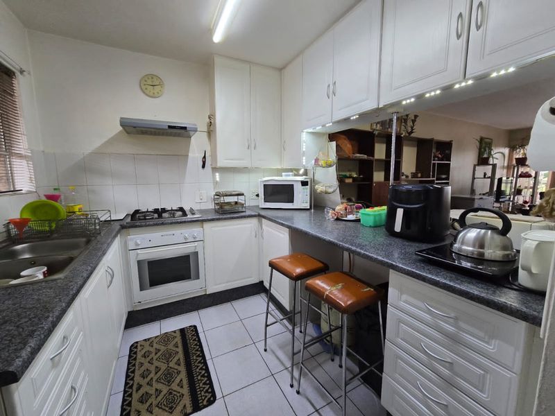 Functional kitchen featuring white cabinetry, granite countertops, a gas hob, electric oven, and a breakfast bar overlooking the living area.