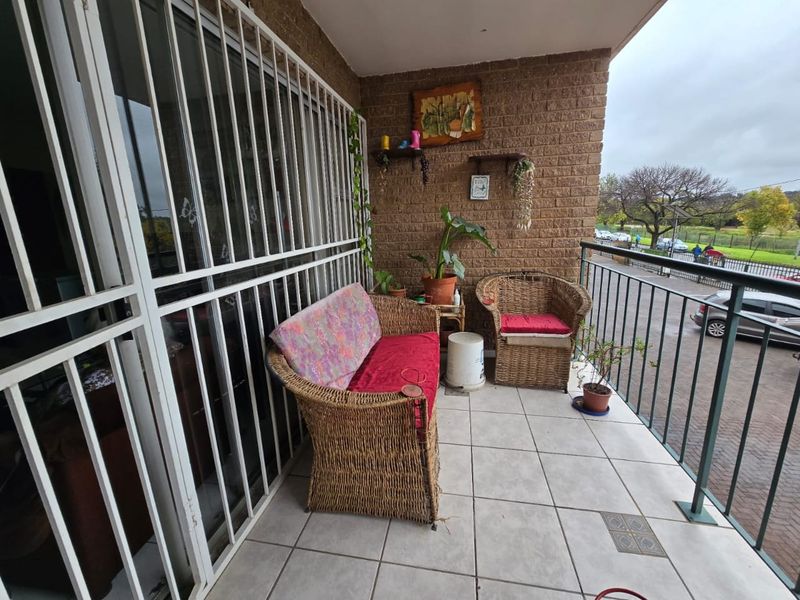 A covered balcony featuring tiled flooring, a brick feature wall, and metal security gates, providing an outdoor space overlooking the street.
