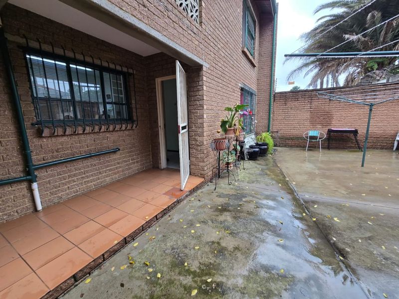A rear exterior view of the flat featuring a brick facade, a tiled patio area, and a paved courtyard space.