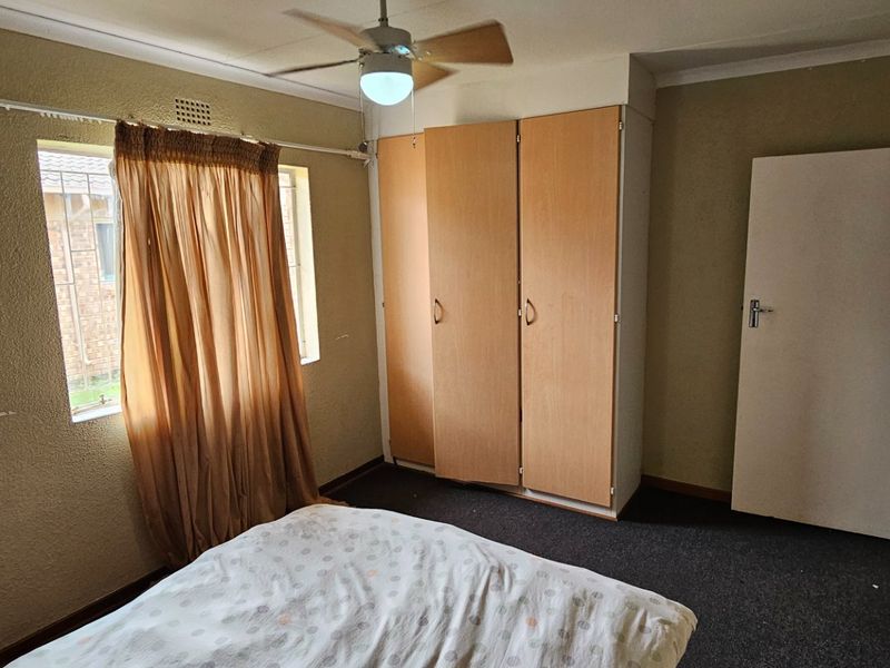 A bedroom featuring built-in wooden cupboards, a ceiling fan, and carpeted flooring, offering a functional space with potential for modernization.