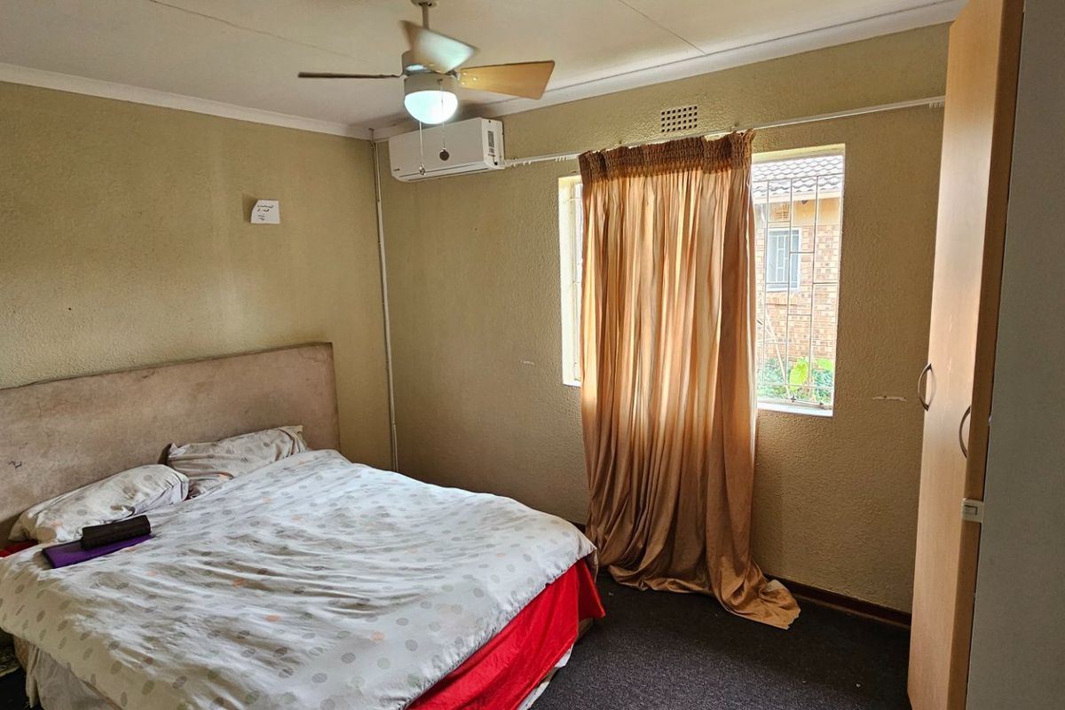 A bedroom featuring a ceiling fan, wall-mounted air conditioning unit, and a window with security bars.
