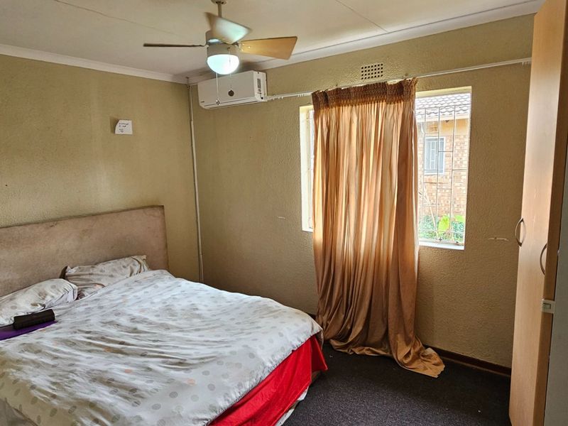 A bedroom featuring a ceiling fan, wall-mounted air conditioning unit, and a window with security bars.