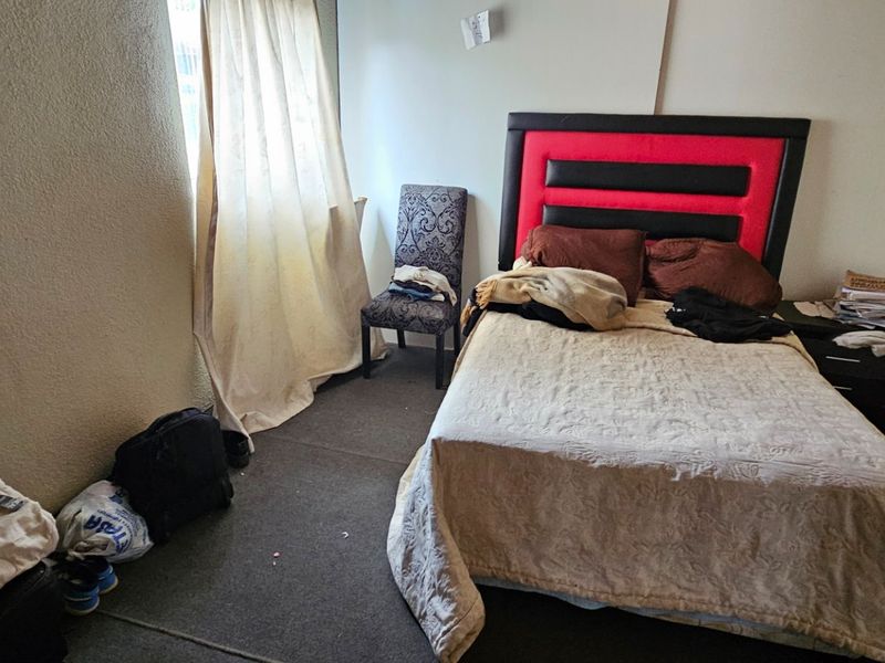 A compact bedroom featuring carpeted flooring and a window with curtains, providing a functional space for rest.