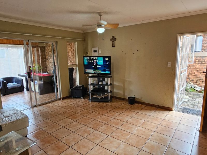 Open plan living area featuring tiled flooring, ceiling fan, and sliding glass doors leading to an enclosed patio area.