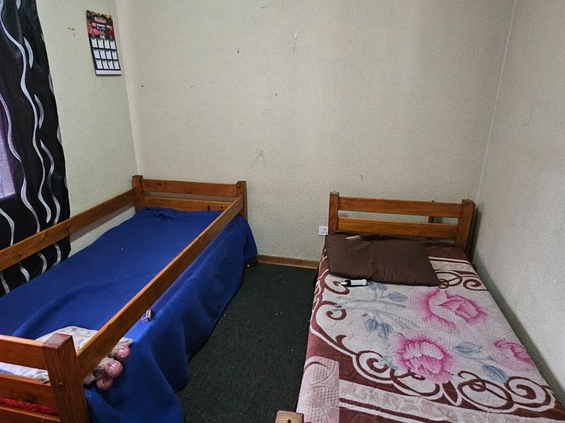 A bedroom featuring two single bed frames, dark carpeting, and a window with curtains.