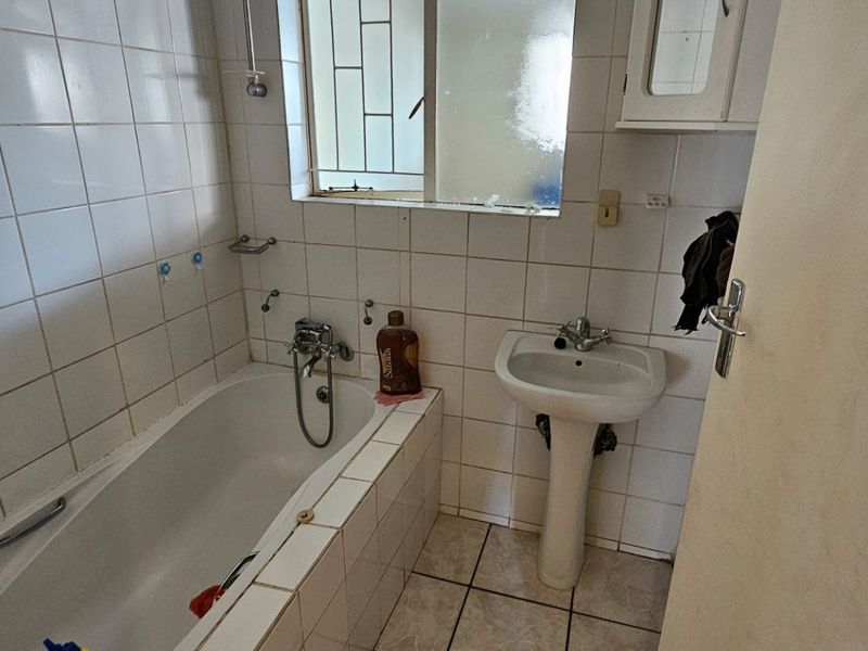 A dated bathroom featuring a standard bathtub with shower mixer, pedestal basin, and tiled walls, requiring modernization to improve functionality and aesthetic appeal.