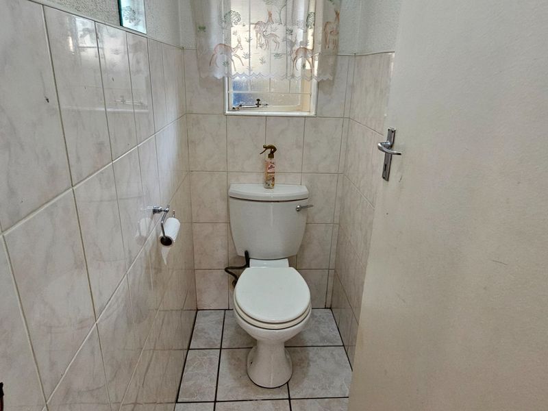A compact guest bathroom featuring tiled walls and flooring, equipped with a standard toilet and a small window for natural light.