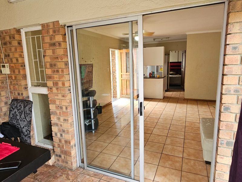 A view from a covered patio through sliding glass doors into an open-plan living and kitchen area with tiled flooring.