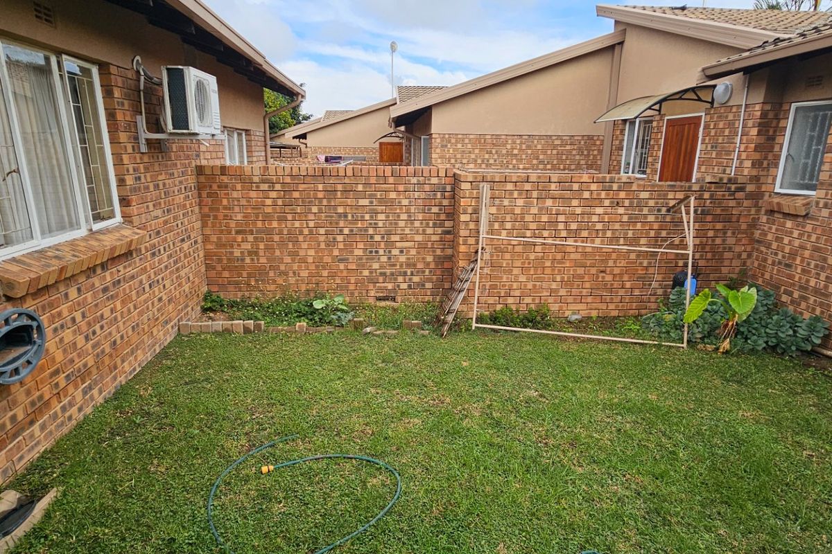 A private rear courtyard featuring a brick-walled garden area with established lawn and exterior wall-mounted air conditioning unit.