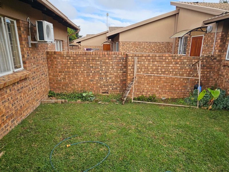 A private rear courtyard featuring a brick-walled garden area with established lawn and exterior wall-mounted air conditioning unit.