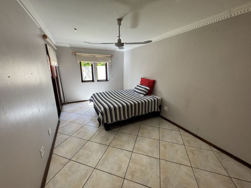 A simple bedroom featuring tiled flooring, a ceiling fan, and sliding door access, providing a functional space with neutral wall finishes.