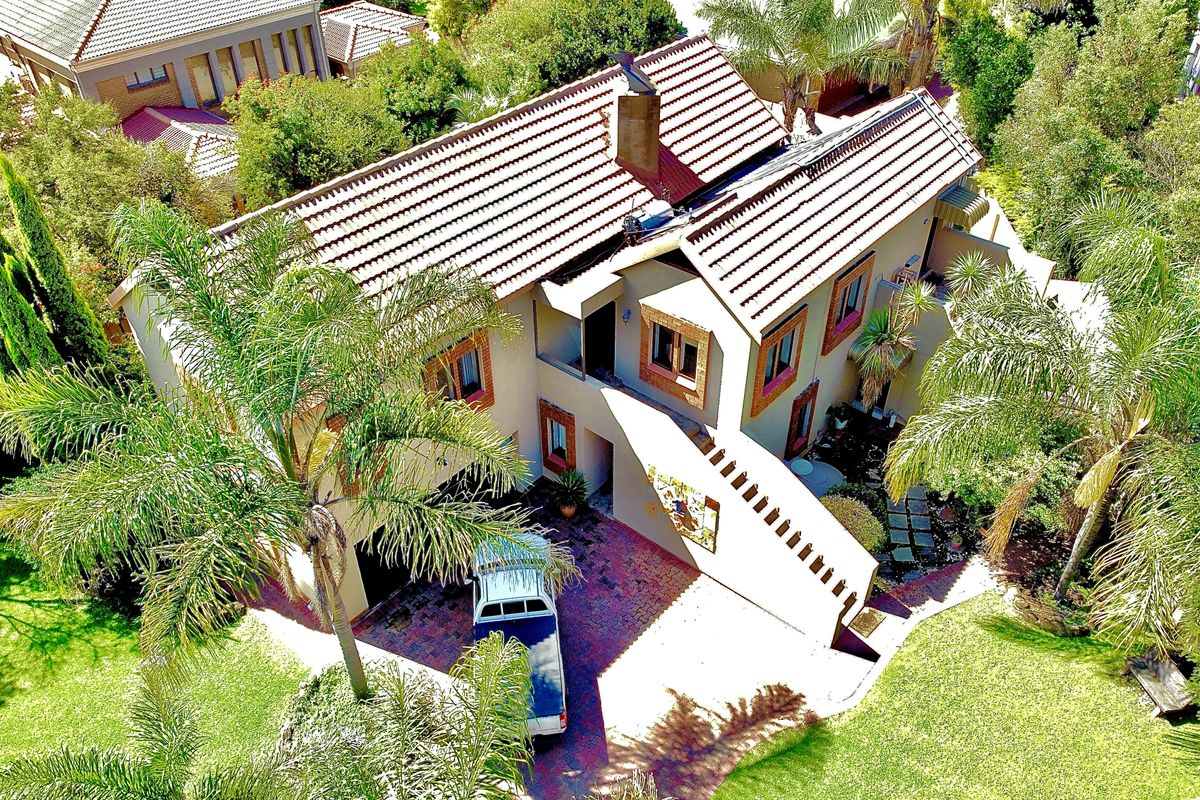 Aerial view of a multi-story residential property featuring a tiled roof, brick driveway, and established garden surroundings.