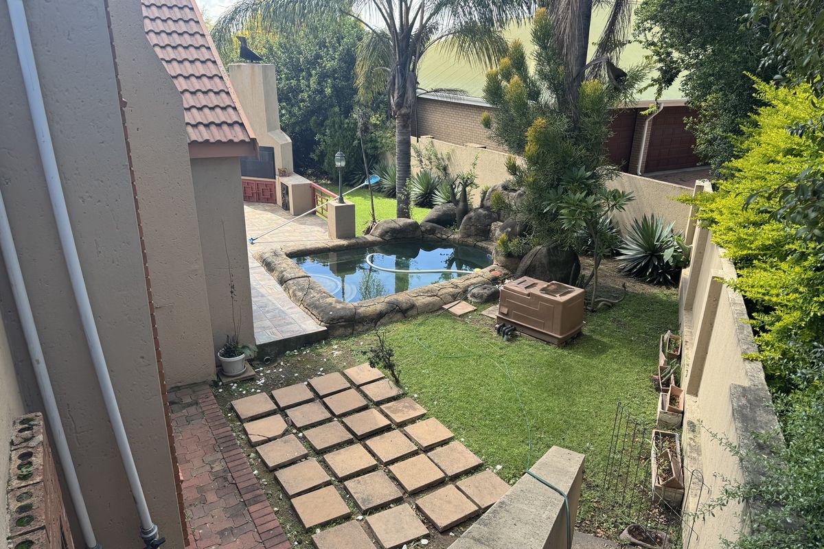 Rear garden area featuring a built-in braai, paved patio, and a rock-edged swimming pool set within a landscaped backyard.
