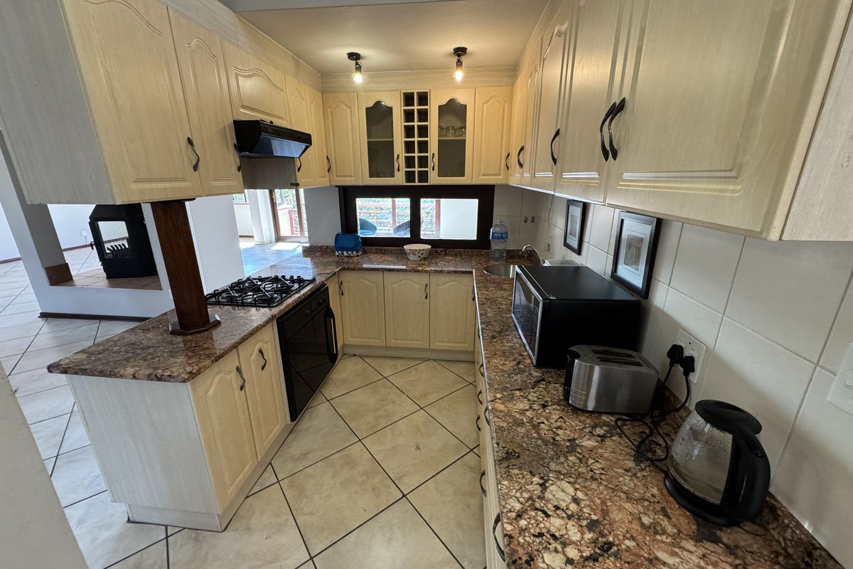 A functional U-shaped kitchen featuring granite countertops, gas hob, extractor fan, and ample built-in cabinetry with tiled flooring and backsplash.