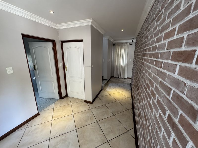 A spacious hallway featuring ceramic floor tiles, an exposed brick feature wall, and decorative crown molding, providing access to multiple rooms.