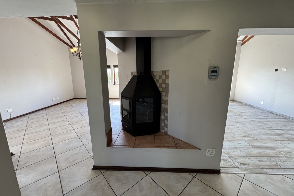 Spacious living area featuring a central freestanding fireplace, tiled flooring, and exposed timber roof trusses, offering a versatile open-plan layout.