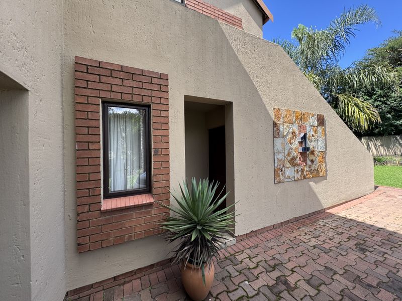 Front entrance area featuring a stucco facade with decorative brickwork, stone cladding, and paved driveway access.