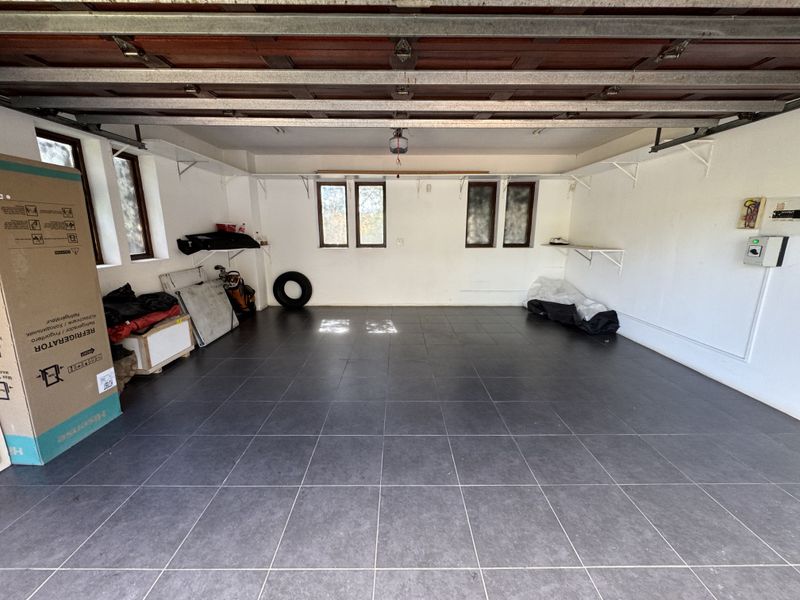 A spacious, clean garage featuring dark tiled flooring, white walls, wall-mounted shelving, and a functional sectional garage door.