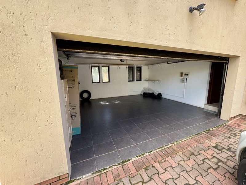A spacious, clean garage featuring dark tiled flooring, fixed shelving, and an external security light, offering versatile storage or parking space.