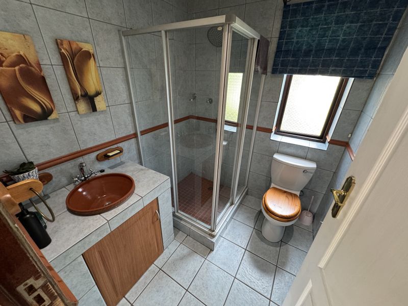 A functional bathroom featuring a corner shower enclosure, a vanity with a vessel sink, and tiled finishes throughout.