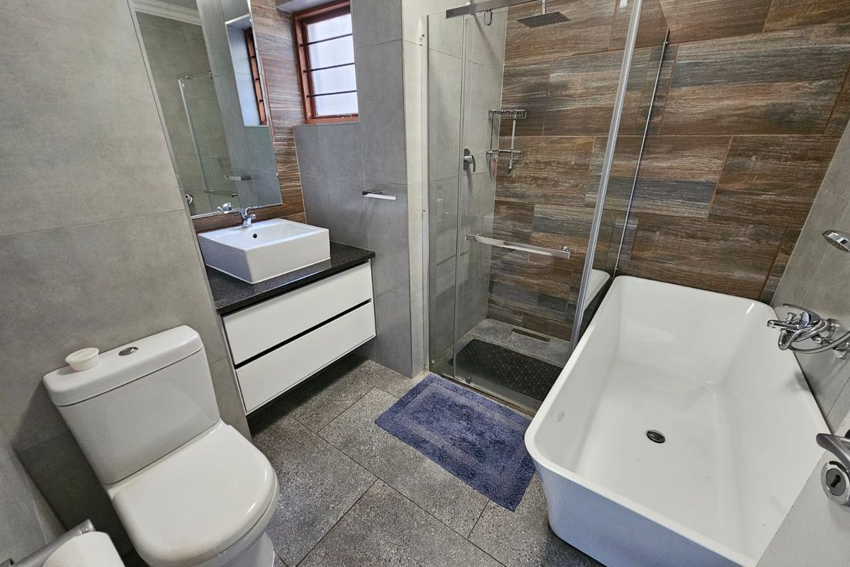 Modern bathroom featuring a freestanding bathtub, glass-enclosed walk-in shower, wall-mounted vanity with vessel sink, and contemporary floor-to-ceiling tiling.