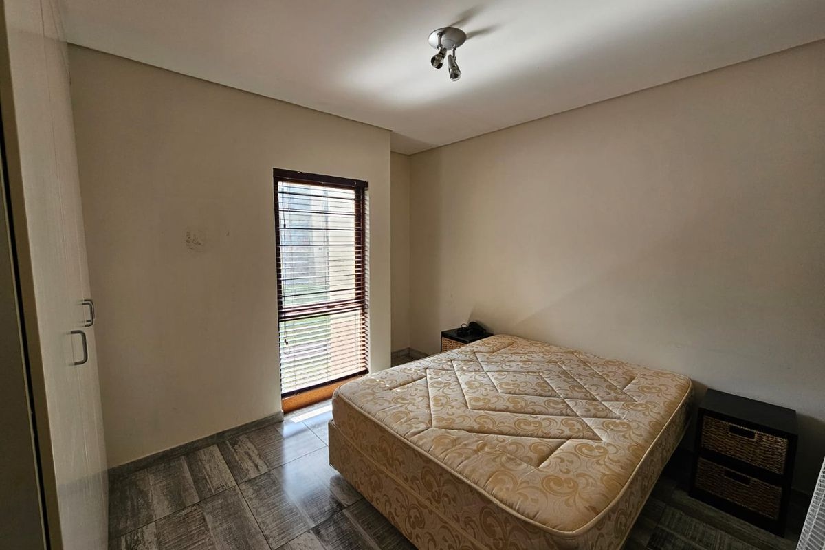 A bedroom featuring tiled flooring, built-in cupboards, and a window fitted with horizontal blinds.