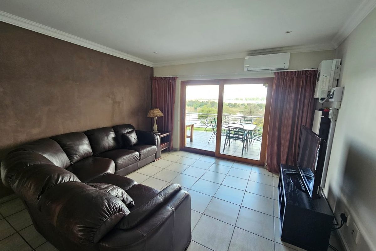 A spacious living room featuring tiled flooring, a wall-mounted air conditioning unit, and large sliding glass doors leading to an outdoor balcony.