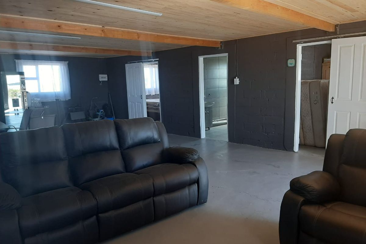 Spacious living area featuring exposed timber ceiling beams, painted blockwork walls, and concrete flooring, with direct access to adjacent rooms.