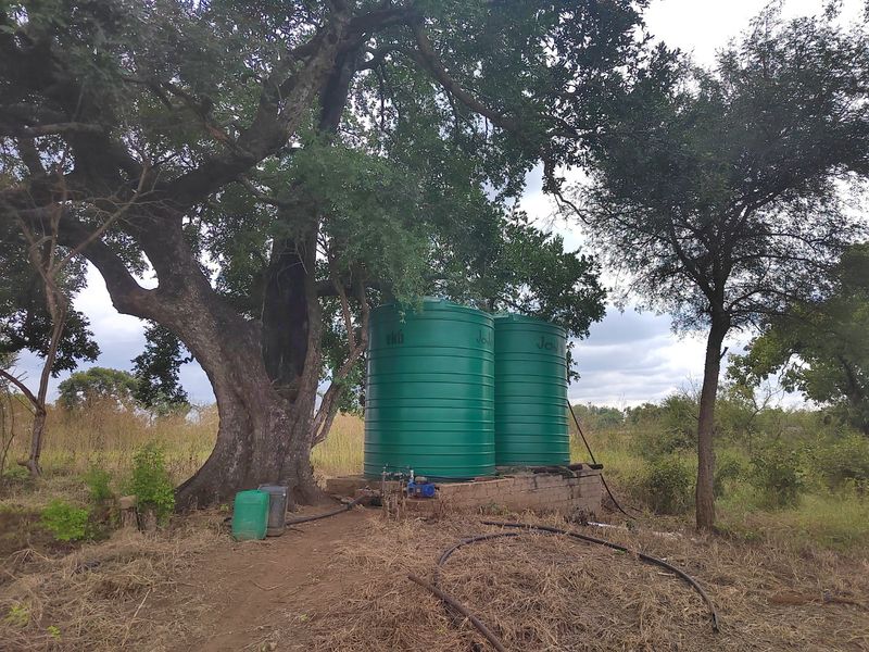 Outdoor utility area featuring two large green water storage tanks mounted on a concrete plinth with associated pump and irrigation infrastructure.