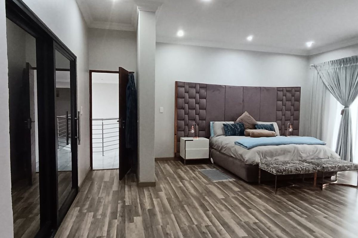 Spacious bedroom featuring wood-look flooring, recessed ceiling lighting, and a large built-in upholstered headboard wall panel.