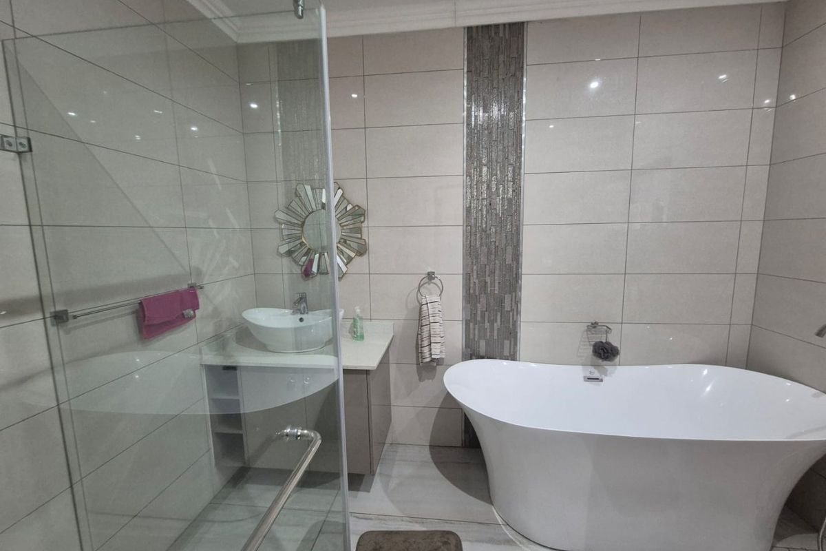 Modern bathroom featuring a freestanding bathtub, glass-enclosed shower, and a vanity with a vessel sink, finished with neutral wall tiles and decorative accents.