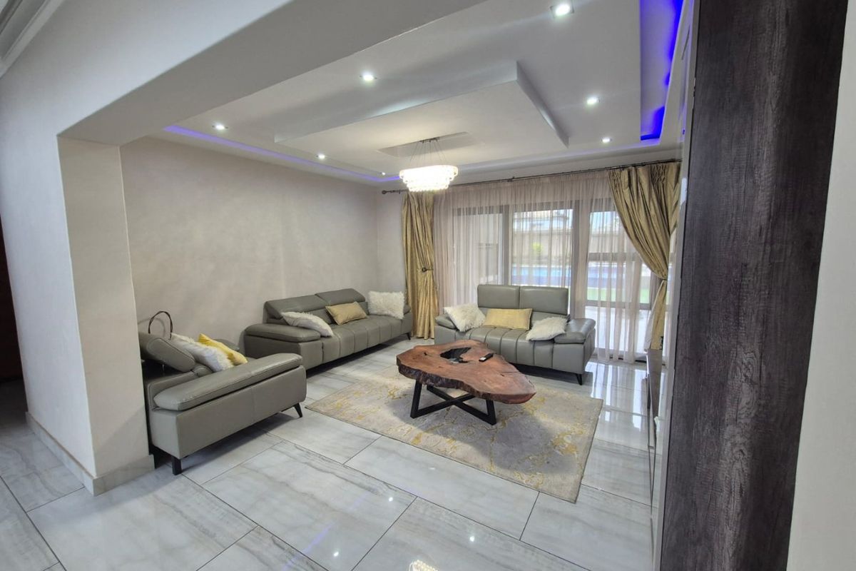 Modern living room featuring polished porcelain floor tiles, a recessed tray ceiling with integrated LED ambient lighting, and large sliding glass doors.