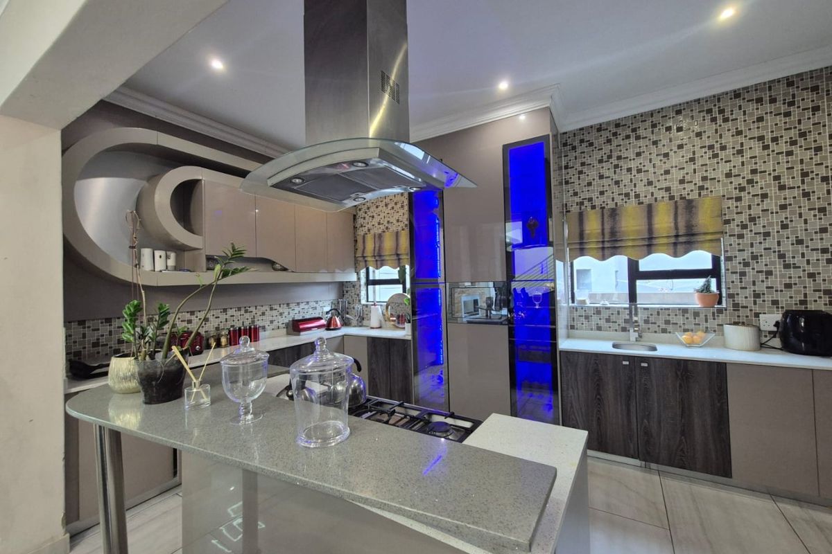 Modern kitchen featuring high-gloss cabinetry, stone countertops, a central breakfast bar, integrated gas hob, and a stainless steel extractor fan.