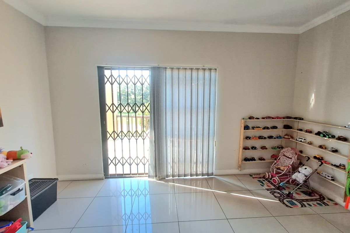 A bright living room featuring large format floor tiles and a sliding glass door with a security gate leading to an outdoor area.