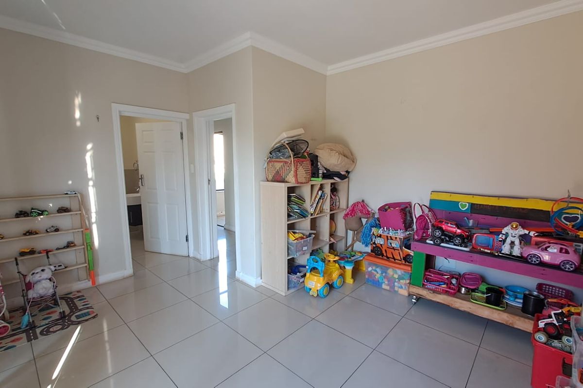 A spacious room featuring neutral tiled flooring and crown molding, currently utilized as a play area with access to adjacent rooms.
