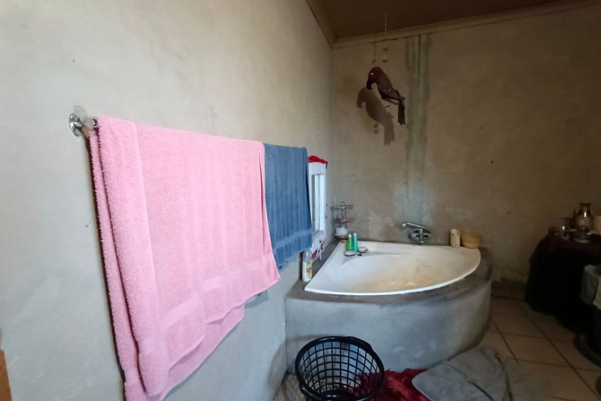 A rustic bathroom featuring a built-in corner bathtub with exposed concrete finish and tiled flooring, requiring cosmetic updates and wall repairs.