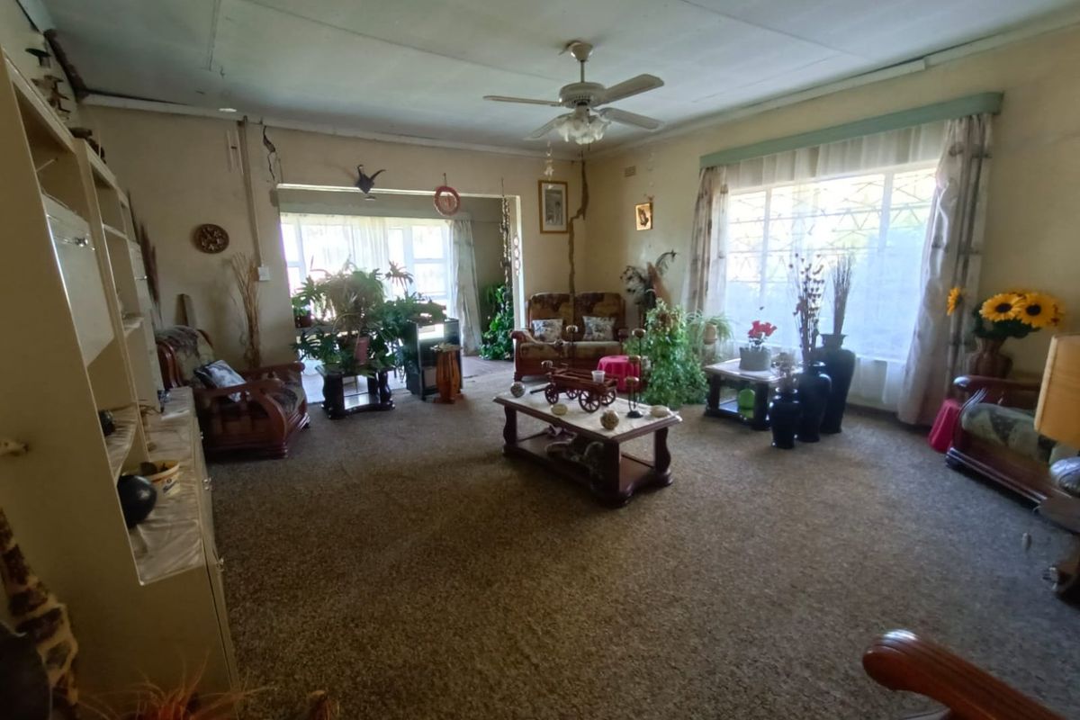 Spacious living area featuring a ceiling fan, large windows with security bars, and carpeted flooring, offering a traditional layout with potential for modernization.