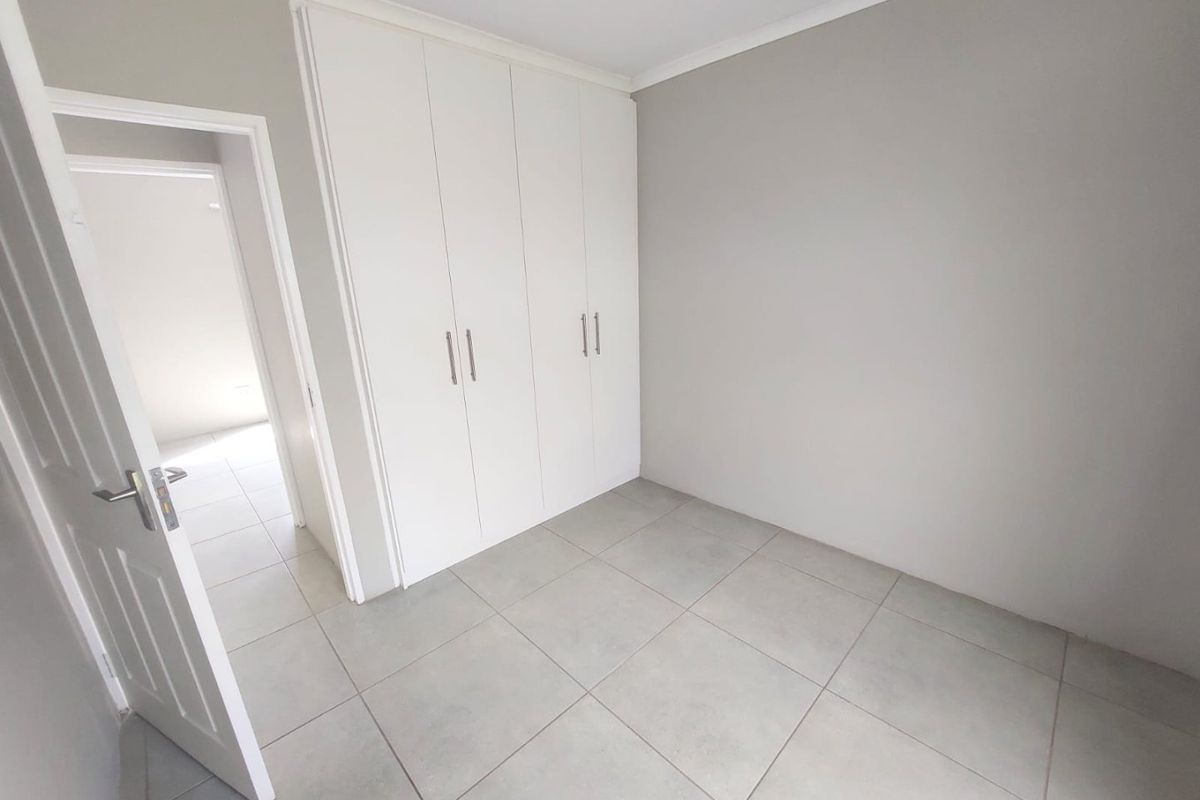 A clean, neutral bedroom featuring built-in cupboards, tiled flooring, and a doorway leading to an adjacent space.