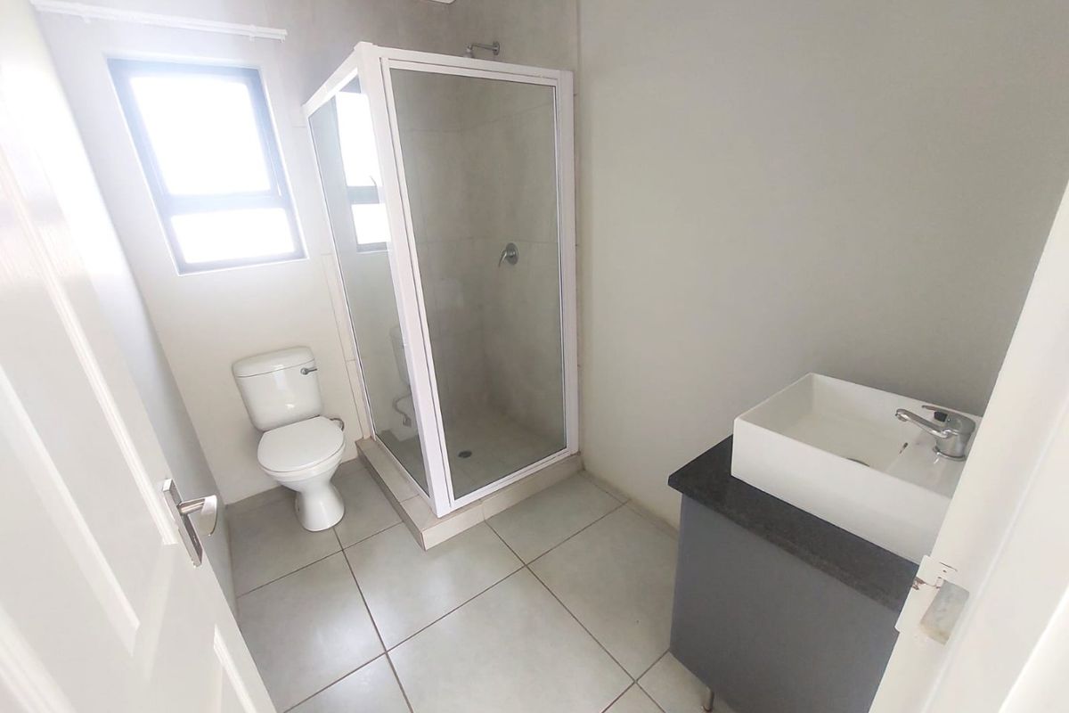 A clean, functional bathroom featuring a glass-enclosed shower, a modern vanity with a basin, and a standard toilet.