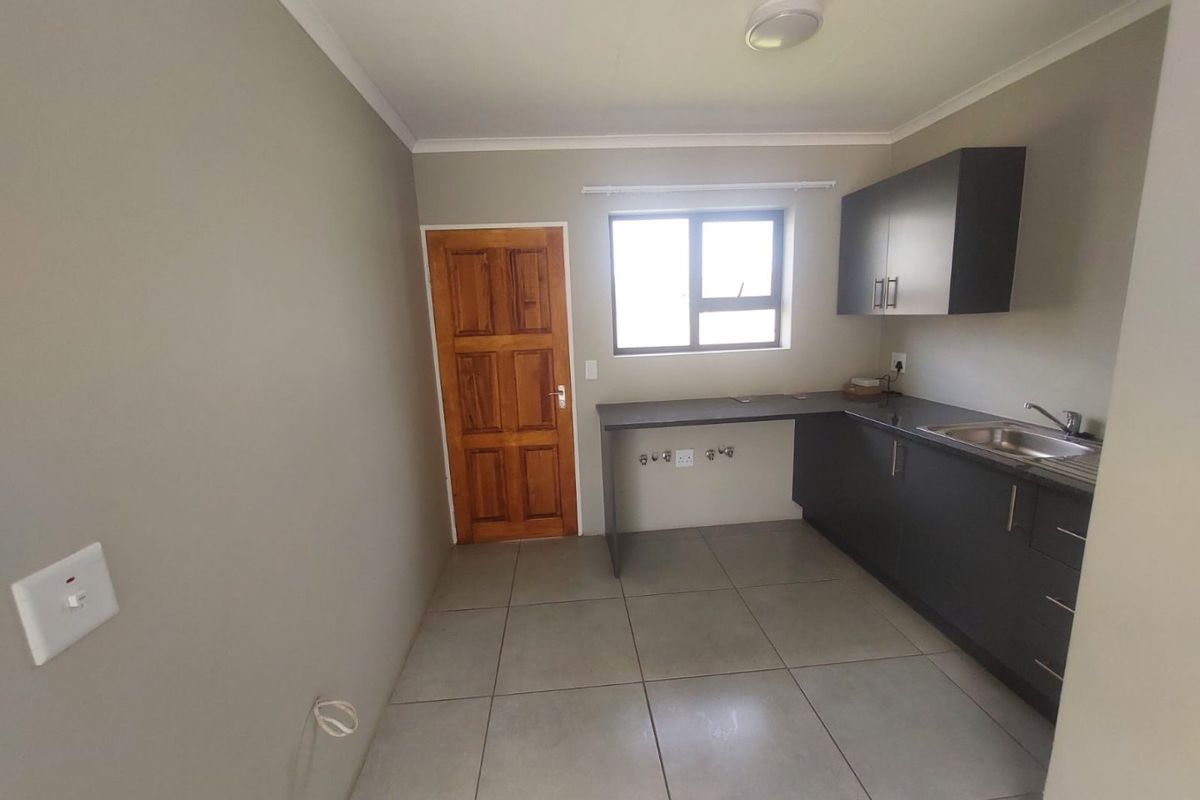 A functional kitchen featuring dark cabinetry, a stainless steel sink, tiled flooring, and a wooden door leading to the exterior.