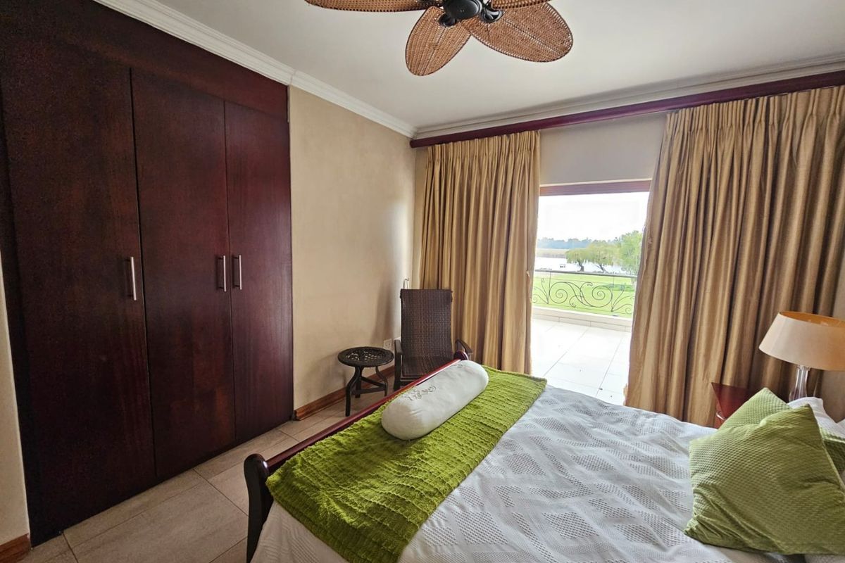 A well-maintained bedroom featuring built-in dark wood cabinetry, a ceiling fan, and sliding glass doors opening onto a private balcony with scenic views.