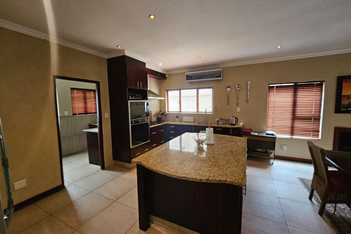 Spacious kitchen featuring dark cabinetry, granite countertops, a central island, and an adjoining scullery area with tiled flooring throughout.