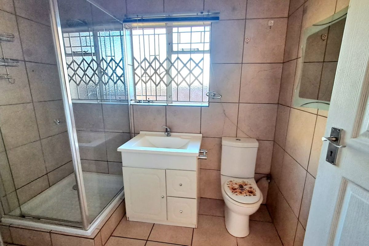 A functional bathroom featuring a glass-enclosed shower, a vanity basin with storage, and a standard toilet, finished with full-height wall tiling.