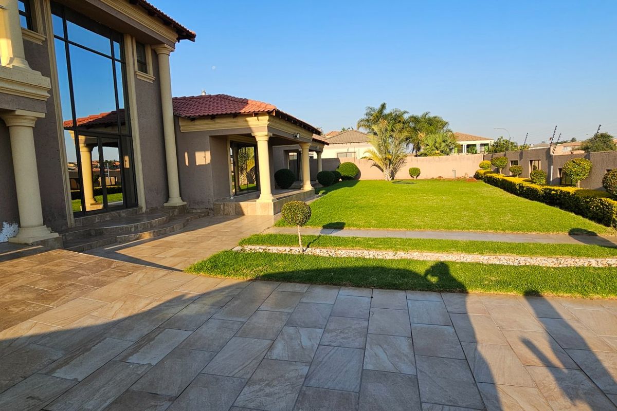 Spacious rear garden featuring a paved patio area, manicured lawn, and established landscaping, providing a private outdoor space for relaxation and entertainment.